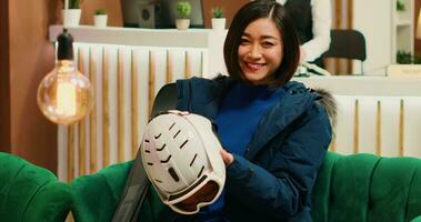 Asian woman preparing for ski session at alpine resort, checking her gear for winter sports on seasonal holiday. Person in outerwear getting equipped for skiing activity down mountain slopes. photo