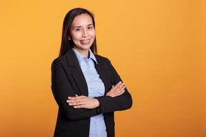 Successful joyful woman standing in arm crossed posing over yellow background, smiling at camera during studio shoot. Smiling asian model with cheerful expression enjoying break time photo