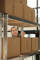 Storage room employee looking at shelves full with boxes, checking products details before preparing customers order in warehouse. Supervisor doing merchandise quality control in storehouse photo