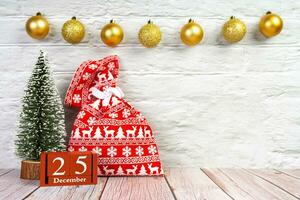 Red gift bag, Christmas tree and red perpetual wooden calendar on white brick background. photo