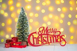 Christmas tree, gift boxes and red wooden lettering Merry Christmas on light bokeh background. photo