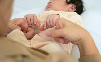 Newborn baby girl or boy holding mother hands. Mom and child on white bed. photo