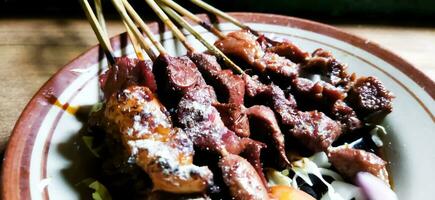 Satay or sate kambing, meat satay served with slice cabbage, red onion, chilli, tomatoes, with soy sauce on plate. Selective focus image photo