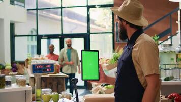 boer Holding tablet met groene scherm in nul verspilling eco markt, gebruik makend van copyspace sjabloon Aan mobiel apparaat staand Bij contant geld registreren balie. klein bedrijf eigenaar presenteert geïsoleerd Scherm. video