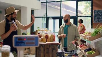 Salesperson in eco store weighs fresh produce and groceries for middle eastern buyer by using modern scale at cash register. Retailer in local shop selling bulk pantry products. video