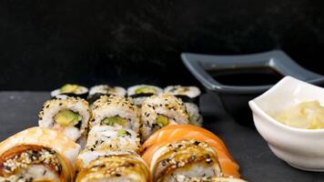 Variety mix of delicious and healthy sushi next to ginger and soy sauce on black stone background video