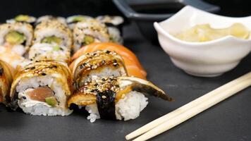 Mix variety of sushi rolls on black stone background next to ginger and soy sauce. Dolly slide shot video