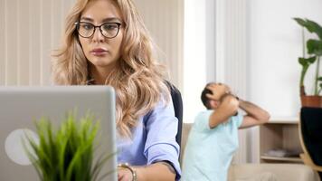 concettuale metraggio di bellissimo libero professionista donna Lavorando su il il computer portatile nel sua Casa mentre sua fidanzato è hoisy nel il sfondo applauso per preferito squadra e disturbare sua opera. dolly 4k metraggio video