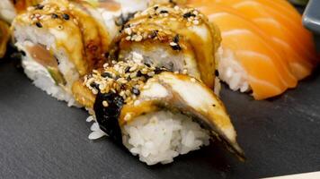 Sushi rotoli nel varietà mescolare su nero pietra piatto. dolly diapositiva parallasse genere metraggio video