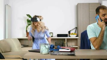 Beautiful blonde woman explores virtual reality while her partner is talking on the cellphone and has a laptop in front, meaning he is working. Dolly slider rack focus 4K footage video