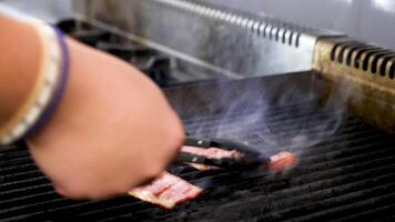 cocinar manos girando dos piezas de ahumado tocino en el parrilla en restaurante video