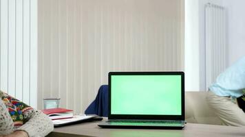 ordinateur avec une vert écran sur le bureau dans vivant pièce tandis que une homme est en jouant une vidéo Jeu sur le console dans Contexte et le femme est parlant sur le téléphone. chariot glissière 4k métrage video