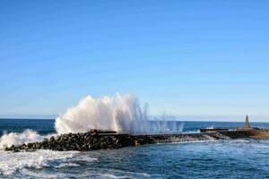 a large wave splashes into the water near a pier photo