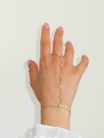 Woman hand wrist wearing golden hand chain set against a white background. photo