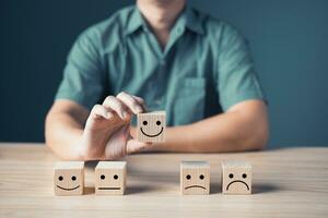 Hand of a businessman chooses a smile face on wood block circle.Customer service experience and business satisfaction survey.rating very impressed.Satisfaction survey concept. photo