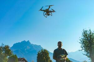 Young man flying drone on amazing mountain landscape. Man operating a drone with remote control taking aerial photos and videos.