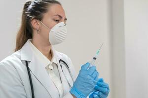 joven atractivo hembra médico preparando vacuna jeringuilla vistiendo preventivo máscara y azul guantes. coronavirus. foto