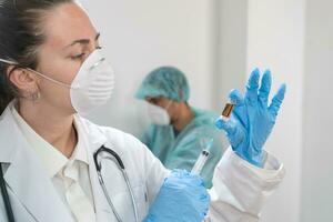 joven atractivo hembra médico preparando vacuna jeringuilla vistiendo preventivo máscara y azul guantes. coronavirus. foto