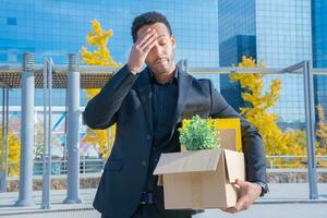 Businessman fired with cardboard box with office supplies standing sad outside office building. photo