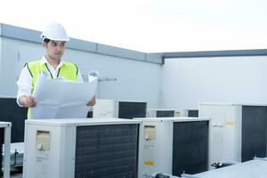 Asian maintenance engineer works on the roof of factory. contractor inspect compressor system and plans installation of air condition systems in construction. Blueprint, inspector, control photo