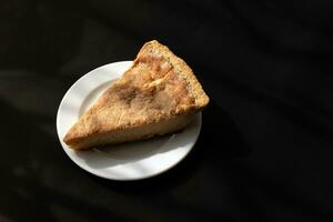 Slice of cheese pie on white plate and black background photo