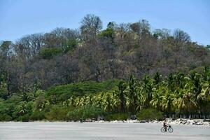 a man riding a bike on a beach near a hill photo