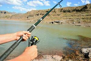 a person holding a fishing rod and reel near a lake photo