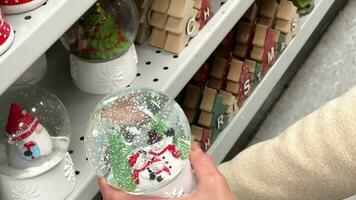 boule de neige dans mains. fermer de une neigeux Noël jouet dans une femme mains. une femme choisit cadeaux pour sa les enfants pour Noël. Noël achats, décorations. de fête accessoires fermer. video