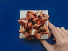 Woman hand holding a gift with gold ribbon bow on blue background photo