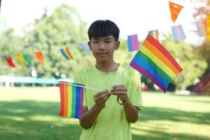 Asian boy holds a rainbow flag in front of a house decorated with rainbow flags during Pride Month to show LGBT pride and identity. Soft and selective focus. photo