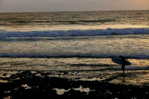 a surfer is standing in the water at sunset photo