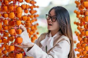 Young woman traveler enjoying dried persimmon hanged on strings to dry a common sight in Da Lat, Vietnam photo