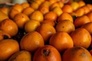 maduro naranja caquis en el mesa en el mercado. un manojo de orgánico caqui frutas a un local agricultores mercado en dalat ciudad, Vietnam. caqui antecedentes. plano poner. foto
