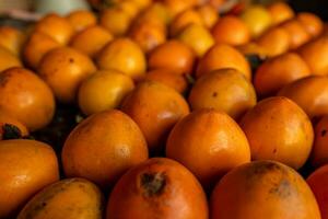 maduro naranja caquis en el mesa en el mercado. un manojo de orgánico caqui frutas a un local agricultores mercado en dalat ciudad, Vietnam. caqui antecedentes. plano poner. foto