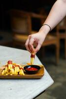 cropped hand dipping potato slice to sauce close up photo