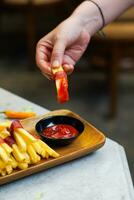 cropped hand dipping potato slice to sauce close up photo