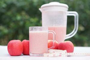 Pink apple fruits smoothie in glass and blender, outdoor background.Concept, healthy beverage for health. Well being and weight loss menu. Homemade refreshing fruit drinks. High fibers, detox. photo