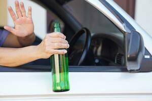 Close up a driver holds bottle of beer in car. Concept, Stop driving while drinking alcohol beverage or whiskey campaign. Illegal and dangerous to drive vehicle that leads to accident photo
