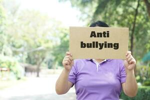 Paper placard with text Anti bullying, was held by a women, stands outside. Concept, campaign for calling everybody to stop bullying each other by using bad word, action, texting or online. photo