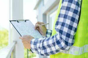 el inspector o ingeniero está inspeccionando la construcción y el aseguramiento de la calidad de la nueva casa usando una lista de verificación. ingenieros o arquitectos o contratistas trabajan para construir la casa antes de entregársela al propietario foto