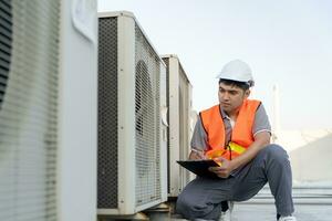 asiático mantenimiento ingeniero trabajos en el techo de fábrica. contratista inspeccionar compresor sistema y planes instalación de aire condición sistemas en construcción. Lista de Verificación, inspector, controlar foto