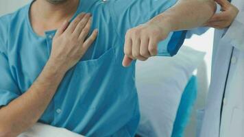 Senior doctor and young male patient who lie on the bed while checking pulse, consult and explain with nurse taking note and supporting in hospital wards. video