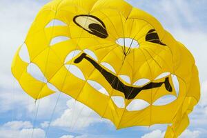 Bright yellow parachute with smile on sky with clouds background. Concept of extreme sport, adventure, challenge, relaxation photo