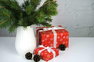 Navidad regalo cajas y abeto ramas en un elegante blanco florero en el mesa. regalos para el nuevo año y Navidad. festivo humor. Copiar espacio. foto