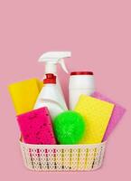 Various detergents and cleaners in the basket on the pink background. Cleaning service concept. Close-up. Selective focus. photo