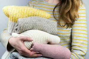 A young woman holds knitted warm sweaters in her hands. Autumn and winter clothes. Decluttering. Donations. Close-up. Selective focus. photo