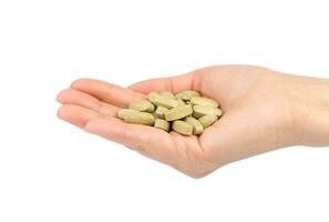 A womans hand holds a green pills isolated on white background. Close-up. photo