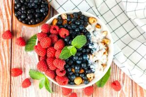 Bowl of granola with rip raspberries, blueberries and yoghurt on a wooden background. Healthy and tasty breakfast in the morning. Top view. photo