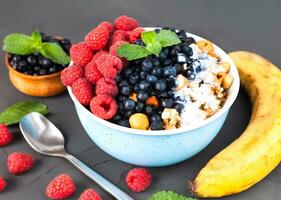 Portion of granola with fresh berries and ripe banana for breakfast on a dark background. Healthy and tasty breakfast. photo