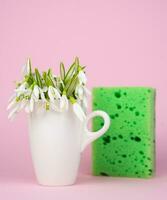 Minimalist composition with spring flowers and kitchen sponge on a pink background. Cleaning concept. Close-up. Selective focus. photo